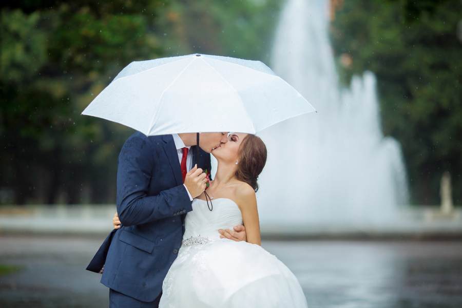 Couple de mariés qui s'embrasse sous un parapluie blanc